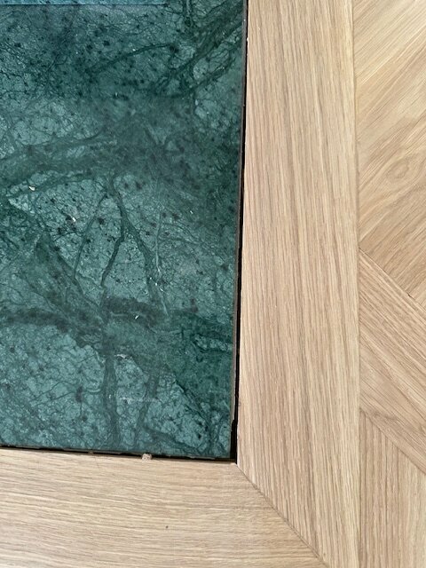 Gap between new oak parquet and green marble plate in front of a fireplace, with small pieces of wood partially filling the space.