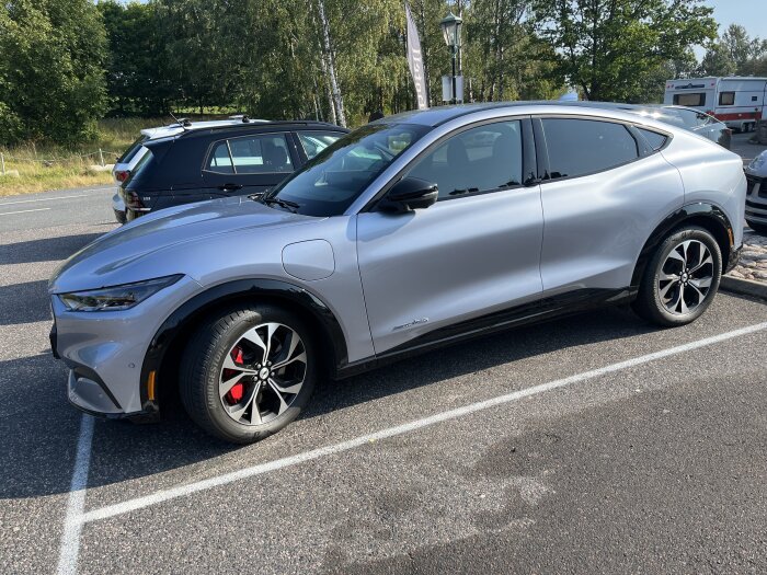 En silvrig SUV parkerad på en parkeringsplats, sedd från sidan. Bakom bilen är det träd och andra parkerade bilar.