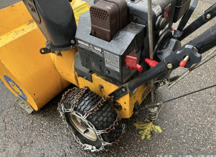 Gul snöslunga av märket Stiga 825 där en av hjulen med snökedjor har en punktering. Maskinen är gammal och sömnens demontering diskuteras.