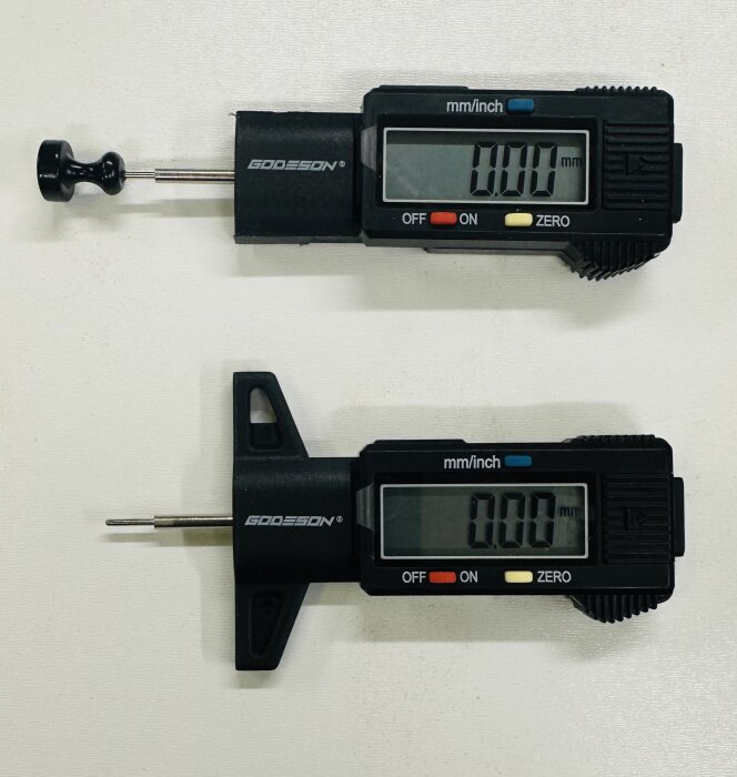 Två digitalmätare liggande på en vit yta, en med en rund magnetisk fot och den andra med en triangelmagnetisk fot. Båda visar "0.00 mm" på displayen.