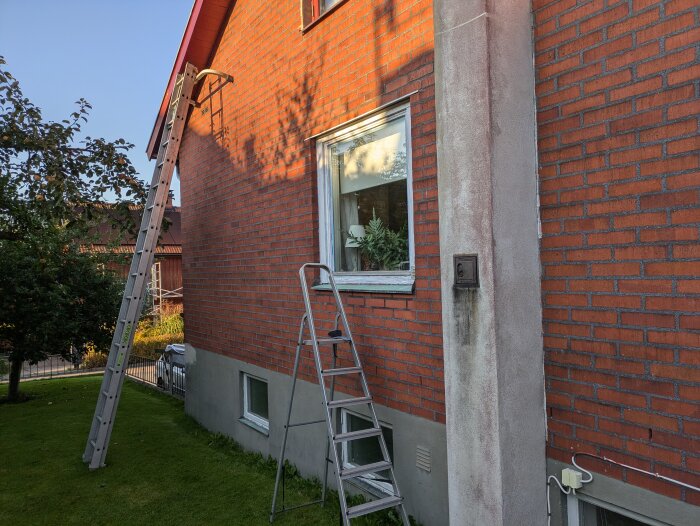 Fasad av ett tegelhus med en stege lutad mot väggen samt en fönsterram som är grundmålad och målad.