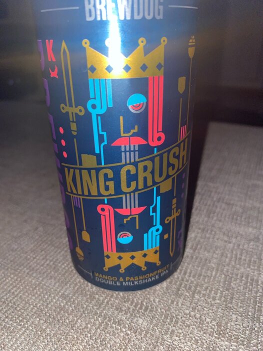 En burk Brewdog King Crush Mango & Passionfruit Double Milkshake IPA med färgglad design, kungakrona och svärd på en matta.