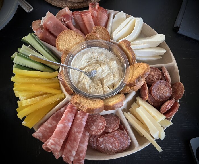 Tapasfat med olika salami, prosciutto, oststavar, brödskivor, gurkstavar, paprikastavar och en skål dip i mitten.