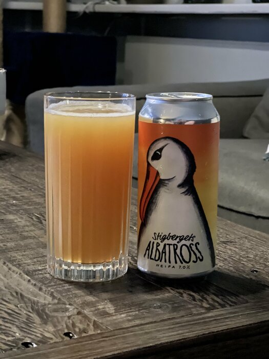 En högglas fylld med ljus, grumlig dryck bredvid en ölburk med etiketten "Stigbergets Albatross NEIPA 7.0%" med en illustration av en albatross.