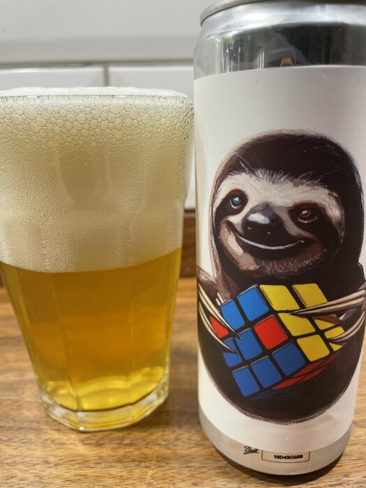 En ölburk med ett leende sengångare som håller en Rubiks kub samt ett glas med öl på en träyta.