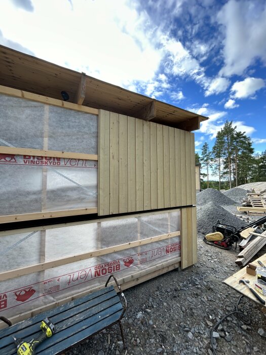 Nybyggt förråd under konstruktion med träpanel från husets överskottsmaterial och vindskydd. Verktyg och byggmaterial spridda runt omkring.