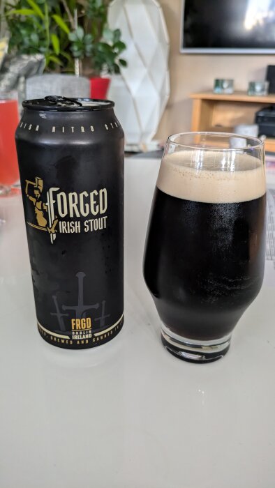 En burk och ett glas med mörk öl av märket Forged Irish Stout på ett soffbord med bakgrund av inomhusmiljö.