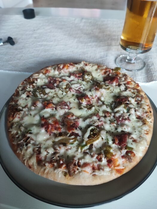 En tallrik med en trimmad Grandiosa-pizza toppad med extra ingredienser bredvid ett glas öl på ett bord.