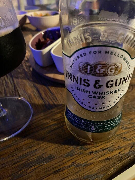 En nästan tom flaska av Innis & Gunn Irish Whiskey Cask öl står på ett matbord bredvid snacks i skålar.