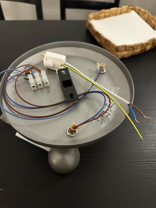 Elektrisk anslutning med flera lösa kablar och en adapter från IKEA, placerad på en rund metallplatta.