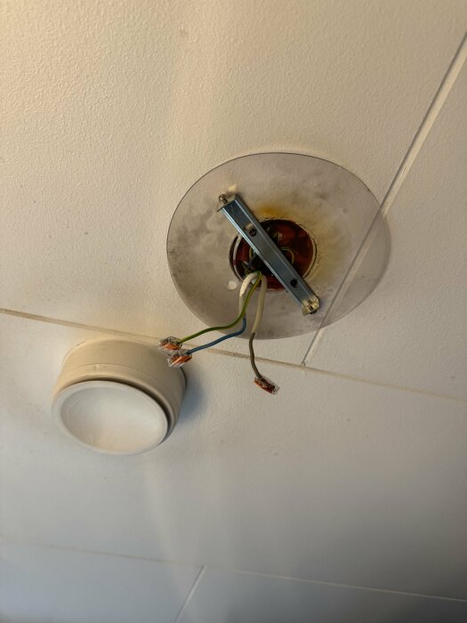 I taket i ett badrum syns en borttagen lampa med kablar och en metallhållare som sticker ut, samt en en sockerbit för inkoppling av elektricitet.