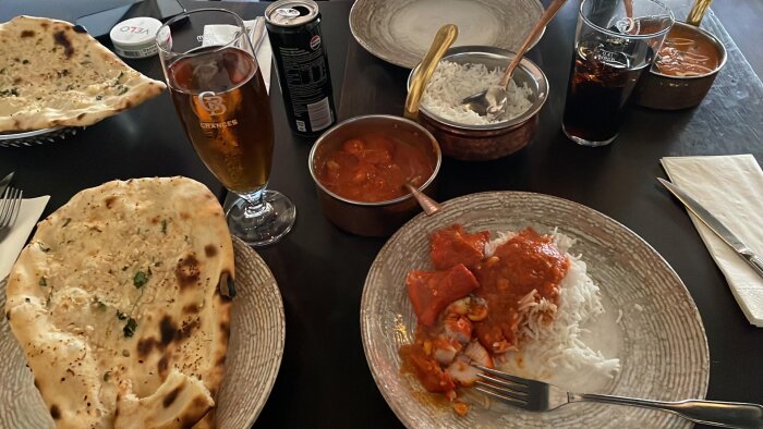 Butter chicken med ris, vitlöksnaan, samt drycker på ett bord.