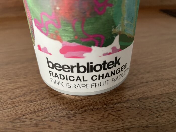 Beerbliotek-behållare med etikett som säger "Radical Changes Pink Grapefruit Radler", placerad på en träyta.