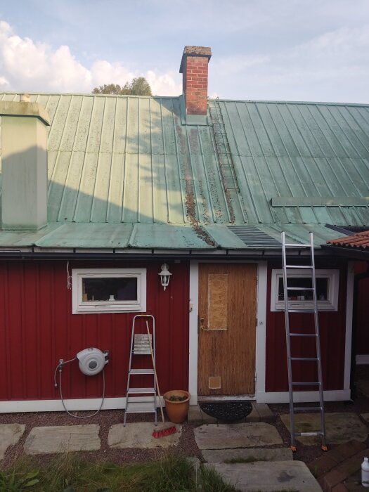 Bild på ett hus från ca 1850 med ett grönt plåttak, tegelskorsten och två stegar. En stege leder upp till tegelskorstenen vid taknocken.