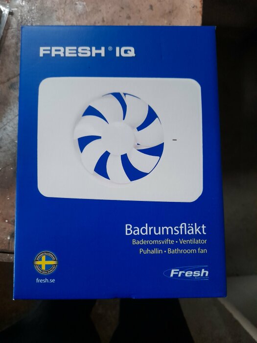 Blå förpackning av märket Fresh IQ som innehåller en badrumsfläkt. Texten på förpackningen inkluderar "Badrumsfläkt" och "Bathroom fan" på olika språk.