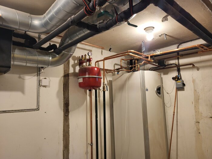 Rörsystem och andra installationer i ett pannrum med synliga kopparrör, en varmvattenberedare, ventilation och en expanstionstank.