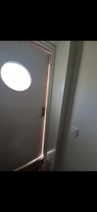 Dörr som släpper in ljus genom springor, särskilt längs neder- och sidosprickorna, med en rund fönsterglugg upptill.