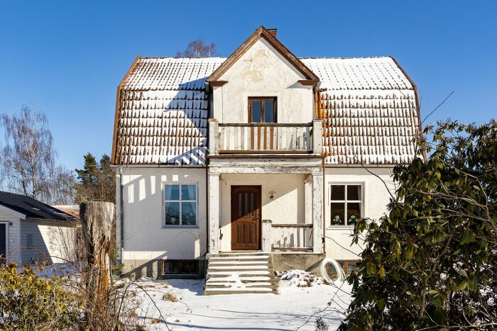 Sekelskifteshus med snötäckt tak, träbalkong och snötäckt trädgård, föreslaget för tillbyggnad och renovering.