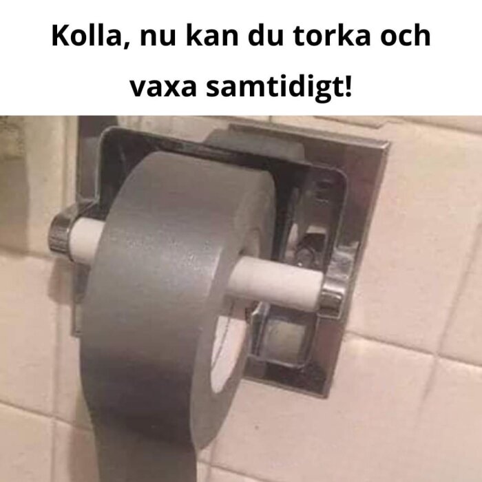 Grå tejprulle i en toalettpappershållare med texten "Kolla, nu kan du torka och vaxa samtidigt!