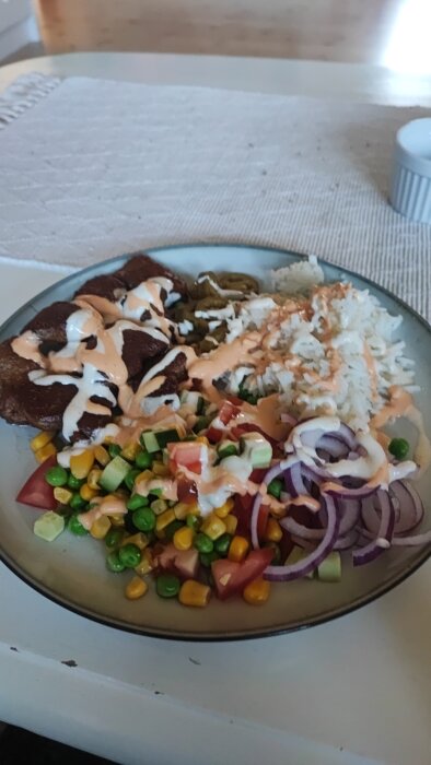 Tallrik med ris, kött, grönsaker (tomat, majs, gröna ärtor, gurka, rödlök) toppade med vit och rosa sås.