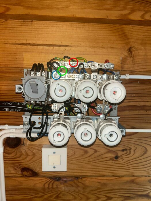 Elcentral i ett gästhus med träribbor i bakgrunden. Kablage är anslutet till markeringar för fas 1, fas 2, och fas 3, med gröna, blåa och röda ringar markerat.