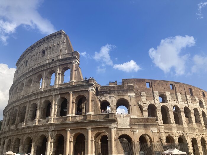 Colosseum i Rom under en klar, blå himmel med några moln.