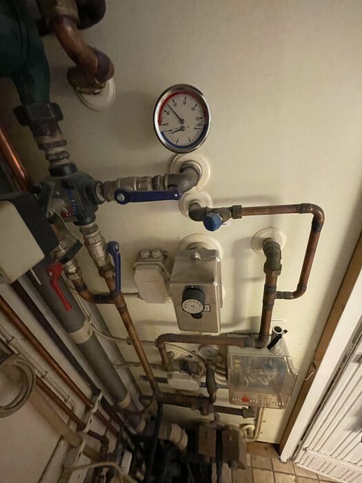 Boiler system with visible pipes, a pressure gauge, and controls mounted on a wall. The boiler model and make are unknown.