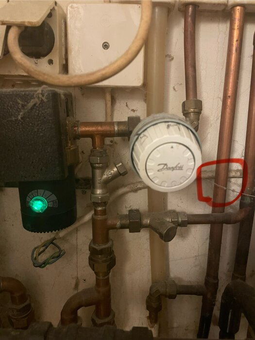 Närbild på pannrum med kopparrör, en grönsvart shuntmotor med lysande display och en termostat märkt "Danfoss". En röd markering runt en kabel.