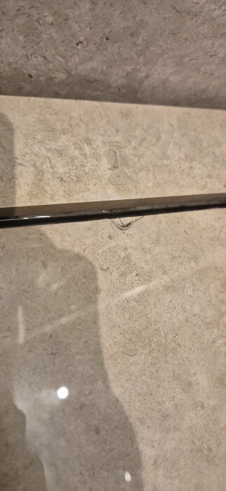 Kantstött kakel nära duschbrunnen. En liten bit av kaklet är avskavd vilket exponerar den underliggande ytan.