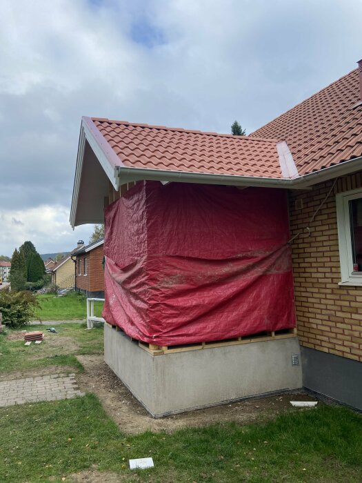 Tillbygge på villa täckt med rödfärgad skyddsplast. Fråga om ventilering mellan tillbyggets och gamla takets luftspalt förklingas i diskussion.