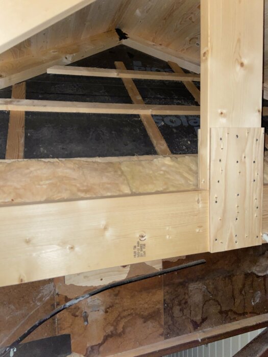 Närbild av en takstol med pågående isoleringsarbete där ventilation och luftspalt är i fokus för tillbyggnad och den gamla takkonstruktionen syns.