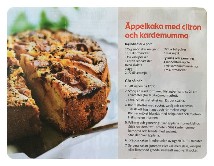 Äppelkaka med citron och kardemumma nyss tagen ur ugnen, toppad med äppelklyftor, kardemumma och sockerblandning. Receptbeskrivning synlig bredvid kakan.