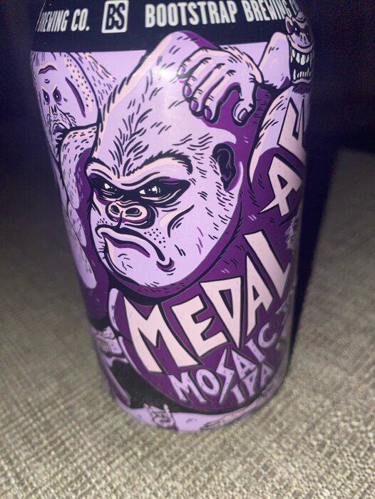 En burk av Medal af Mosaic IPA från Bootstrap Brewing Co. med lila etikett som visar en tecknad apa och texten "Medal af Mosaic".