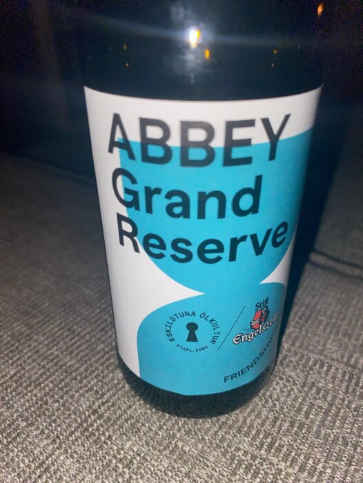 Närbild på en ölflaska med etiketten "ABBEY Grand Reserve". På etiketten finns loggan för Eskilstuna ölkultur och texten "Etab. 2006".