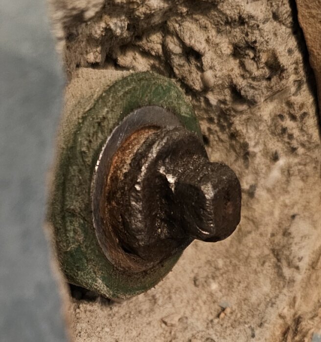 Rostig bult och mutter inskruvad i betongvägg fotograferad på nära håll.
