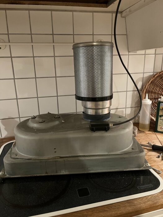 Köksfläkt och ventilationsrör över en spis med vit kakelvägg i bakgrunden.