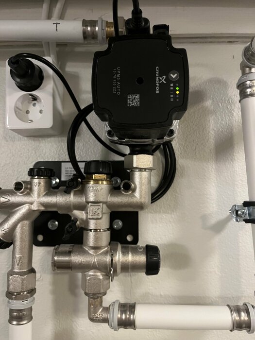 Närbild på en Grundfos vattenpump och relaterade röranslutningar i ett golvvärmesystem.