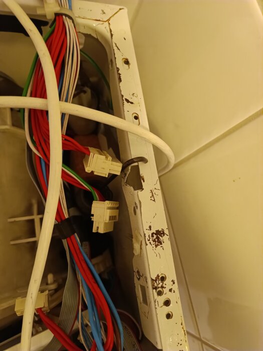 Öppen tvättmaskin med synliga elkablar och kontakter, samt rostiga detaljer på insidan av en Hoover-tvätthanteringsenhet.