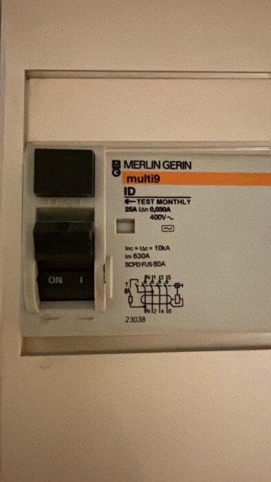 Bild av en elektrisk komponent med etiketten "Merlin Gerin multi9". Informationspanel visar: 25A, 0,030A, 400V samt "TEST MONTHLY".