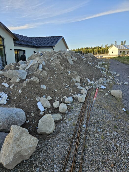 En stor hög med fyllnadsmassor och stenar framför ett hus i Gemla, Växjö Kommun, omgiven av andra bostäder och skogslandskap i bakgrunden.