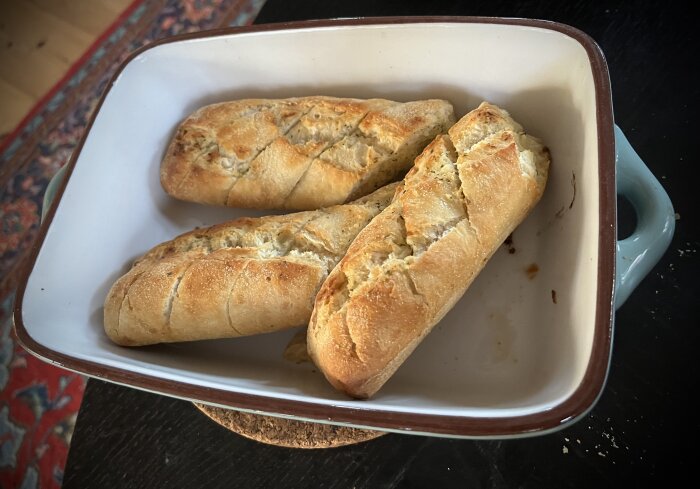 Tre vitlöksbröd ligger i en vit ugnsform på ett bord, redo att serveras som tillbehör.