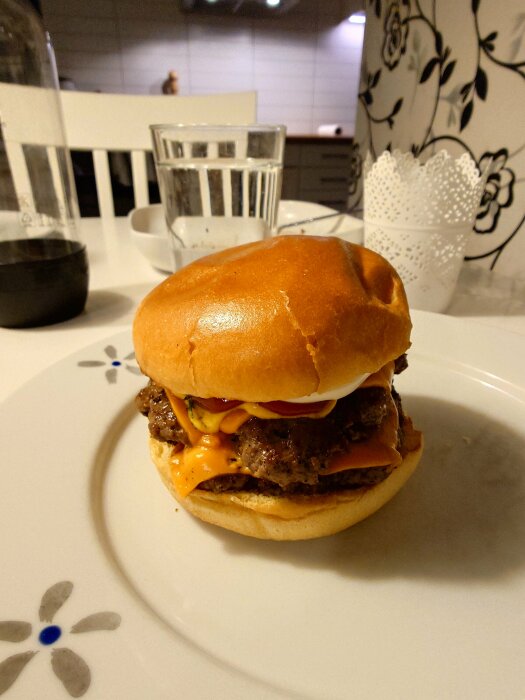 Smashburgare med Väddö cheddar, dillpicklad gurka och tryffelmajo, serverad på ett vitt keramiskt fat på ett bord.