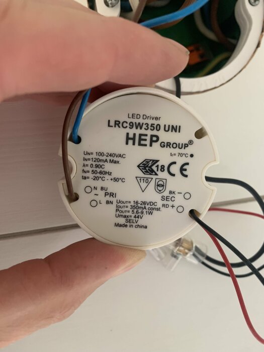 En närbild på en elektronisk LED-driver med märkning "HEP Group LRC9W350 UNI" och specifikationer för koppling och strömstyrka, hållen av en hand.