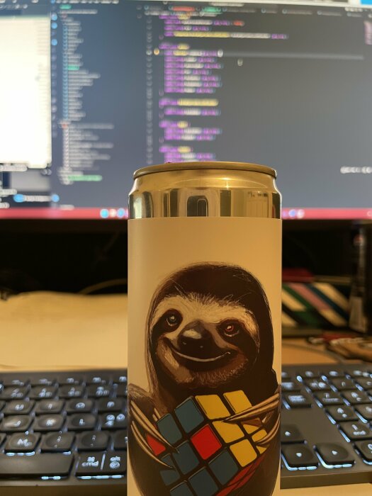 Ölburk med en bild av en sengångare som håller i en Rubiks kub, framför en dator med programmeringskod på skärmen i bakgrunden.