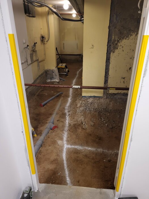 Basement renovation with exposed ground and visible plumbing pipes; area marked with white lines for concrete slab installation.