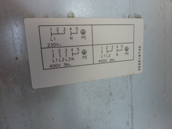 Etikett med spiskopplingsinstruktioner för 230V och 400V med terminalnummer och L1, L2, L3, N och PE markeringar på en metallpanel.