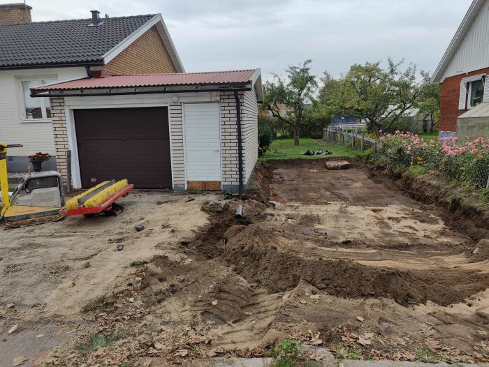 Garage med sprucken vägg, grävd uppfart och synlig jord, pågående arbete för att förbättra grundläggning och dränering.