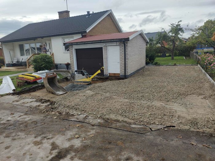 Bilden visar ett garage med sprickor i marken framför. Ny uppfart med grus och byggmaterial på platsen. Ett hus syns i bakgrunden.