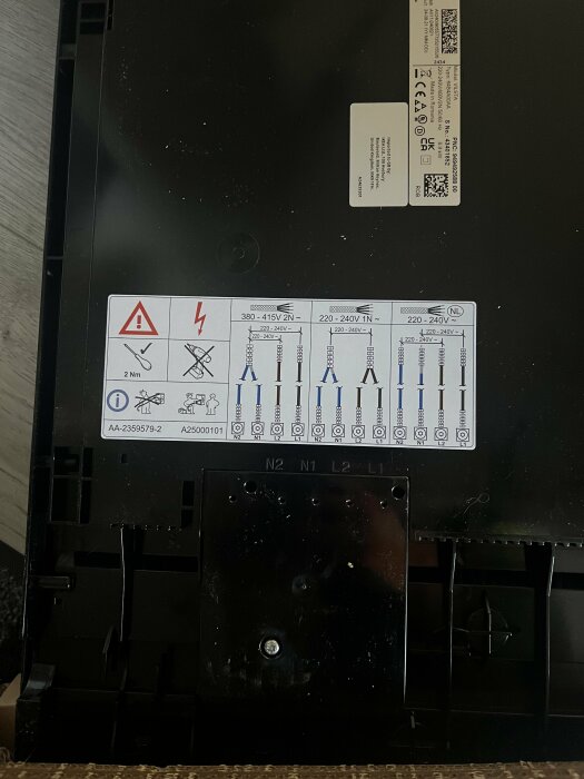 Instruktionsetikett för anslutning på baksidan av IKEA induktionshäll, med varningssymboler och elektriska specifikationer.