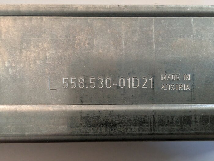 Metallskena med text "L 558.530-01D21 Made in Austria" präglad på ytan.